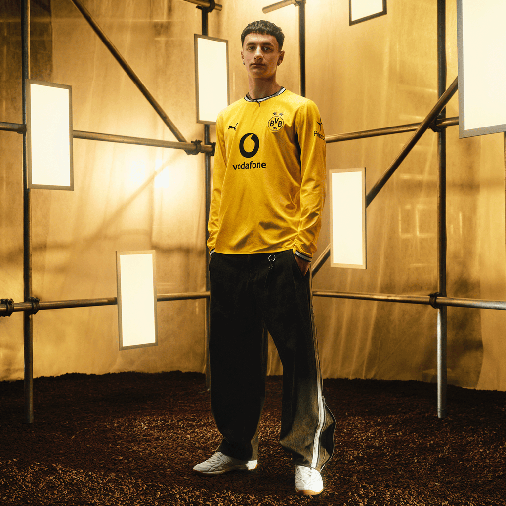 Le maillot domicile à manches longues du BVB pour la saison 2026/27, aux couleurs noir et jaune, orné du logo PUMA, du logo Vodafone et de l'emblème du BVB, présenté par un mannequin devant un décor moderne.