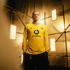 Le maillot domicile à manches longues du BVB pour la saison 26-27, de couleur jaune, avec un col noir et le logo PUMA, ainsi que Vodafone en tant que sponsor, présenté sur un fond moderne.