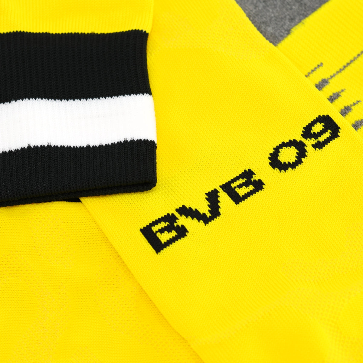 Nahaufnahme eines gelben BVB-Stutzen mit schwarzem und weißem Streifen sowie aufgesticktem BVB 09 Logo, ideal für Borussia Dortmund Fans.