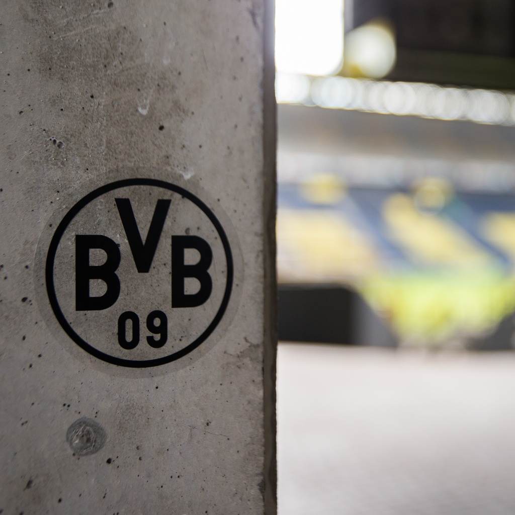 Un autocollant noir « BVB 09 » sur un mur en béton, avec en arrière-plan une image floue du SIGNAL IDUNA PARK.